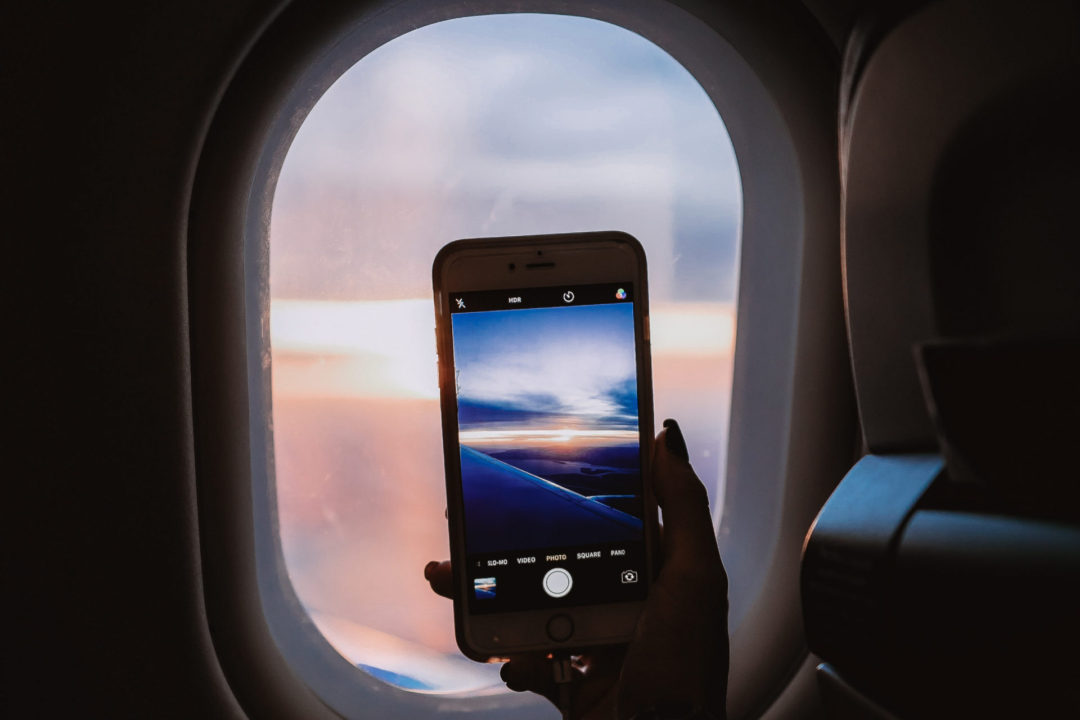A woman's hand holding up an iphone to an airplane window