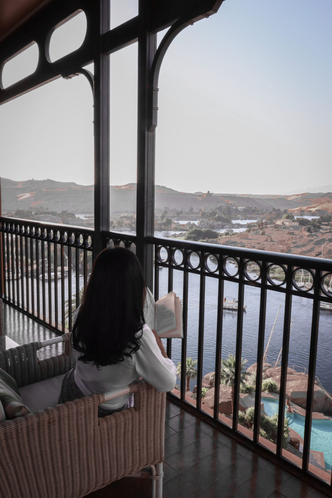Travel Blogger Jordan Gassner reading a book on a balcony overlooking the Nile and pool at the Sofitel Legend Old Cataract Hotel