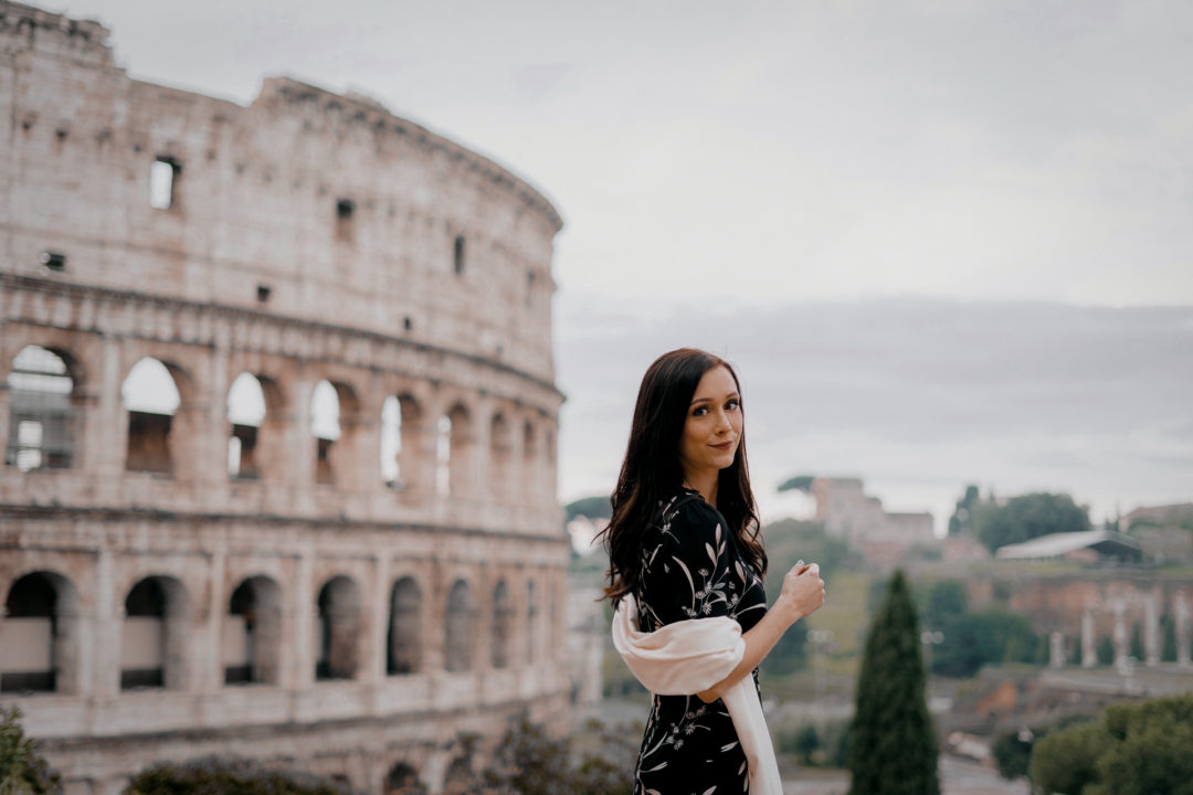 Jordan Gassner at a viewpoint in front of the Coliseum in Rome while wearing a black dress and cream scarf