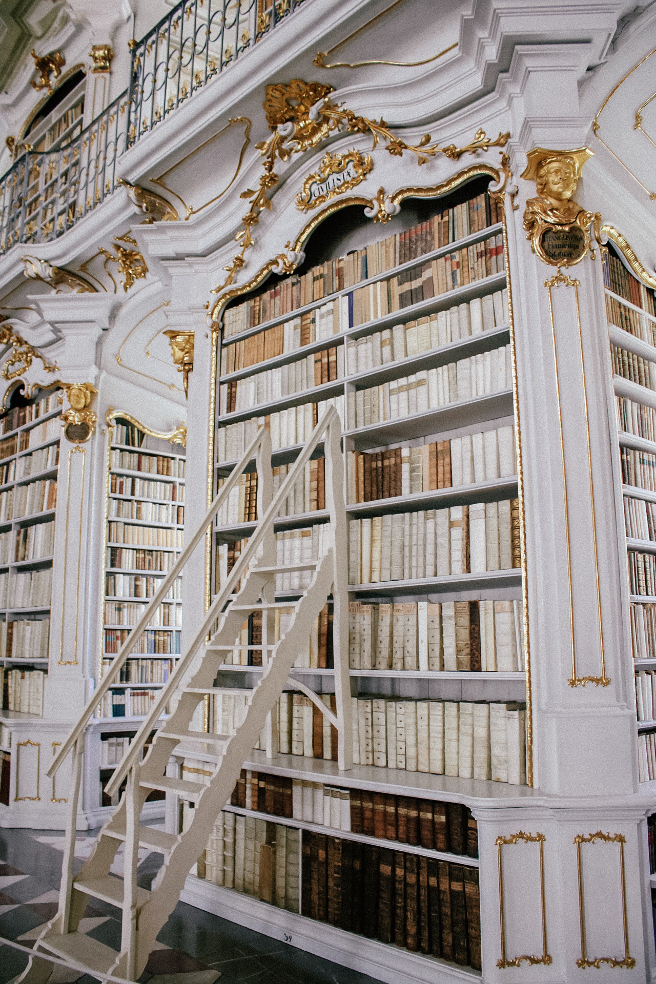 A set of moveable stairs resting against one of the many white bookcases at Admont Abbey, the largest monastic library in the world.