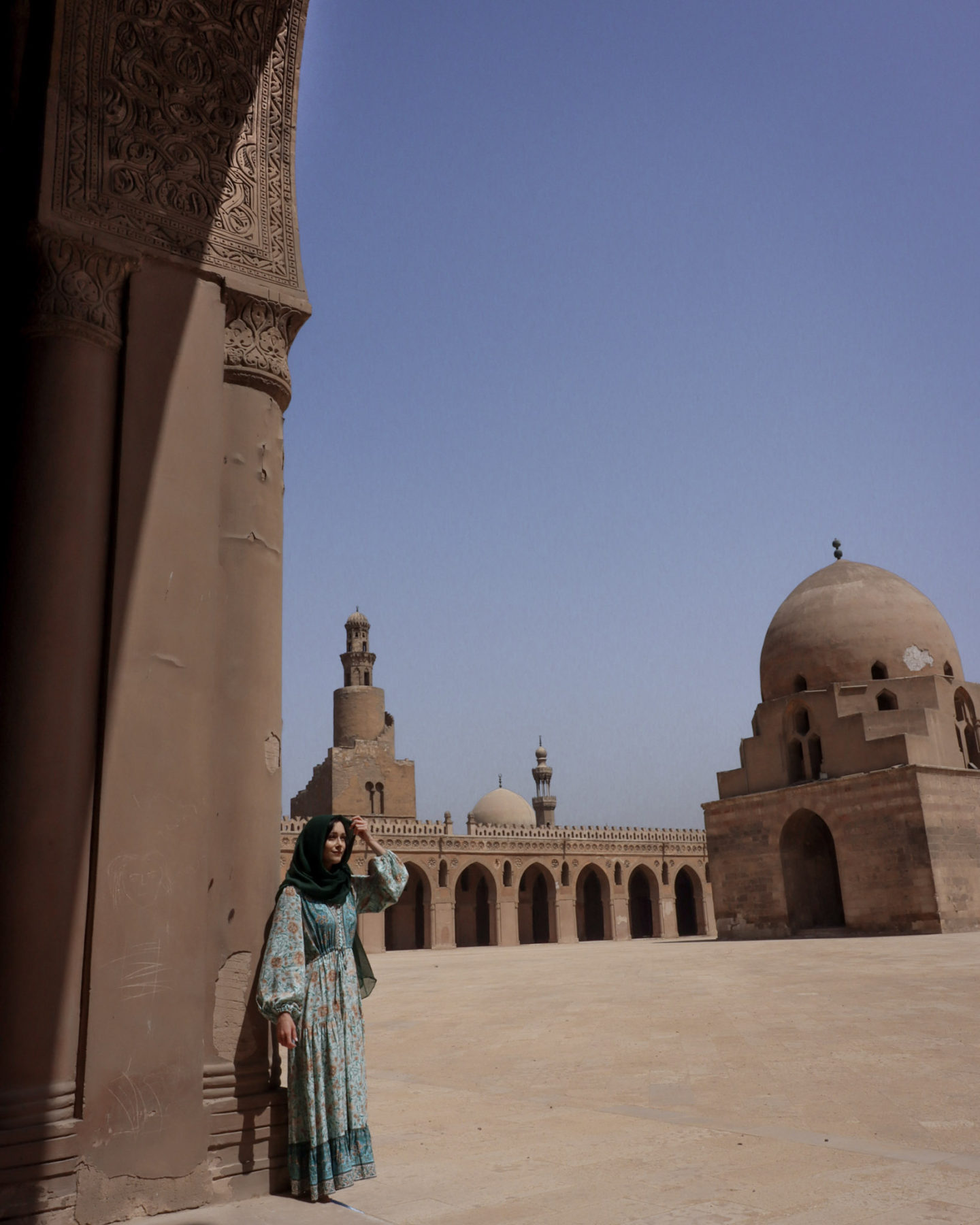 Solo Female Traveler in a turquoise dress and hunter green head scarf inside one of the Must-See Cairo Mosques: The Mosque of Ibn Tulun
