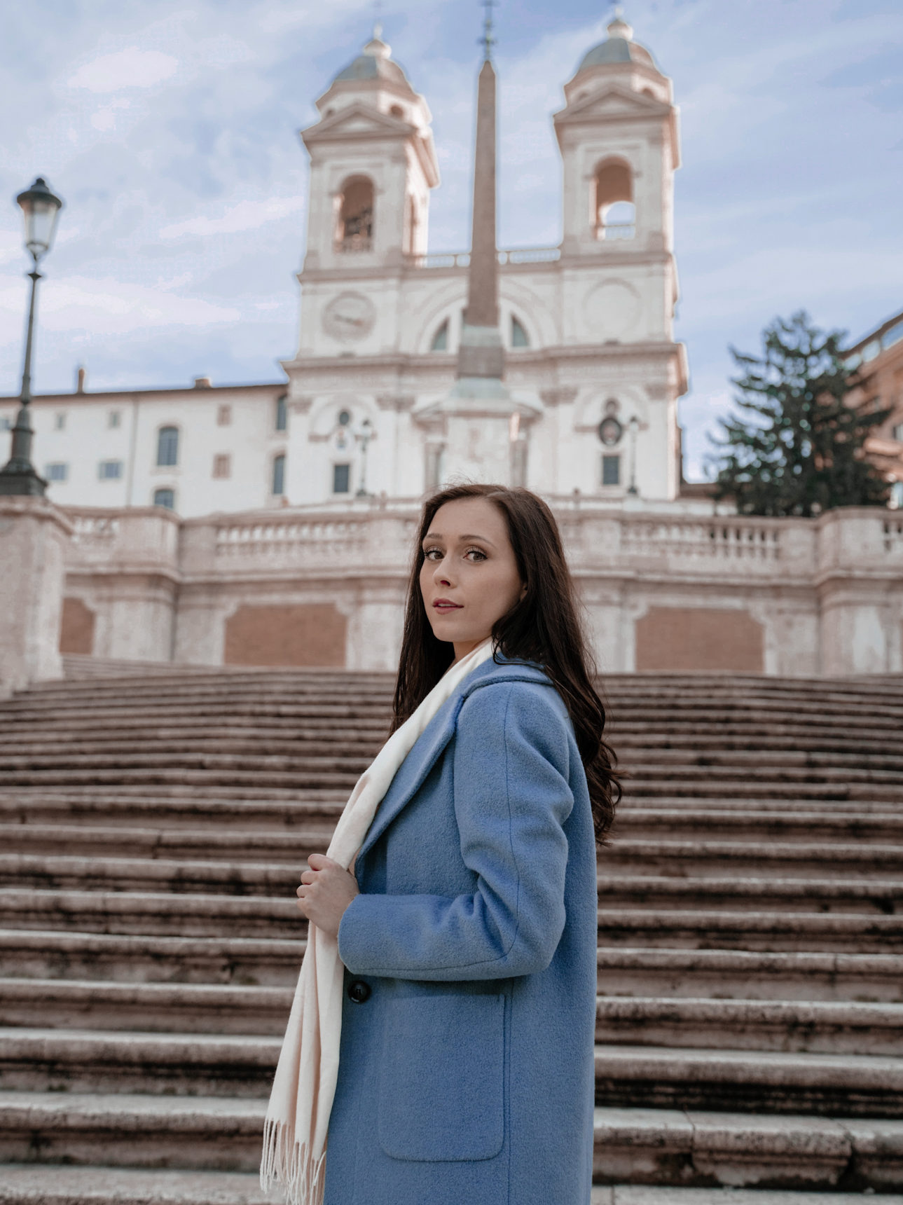 Jordan Gassner wearing a sky blue peacoat and cream scarf in front of the rarely empty Spanish Steps in Rome, Italy