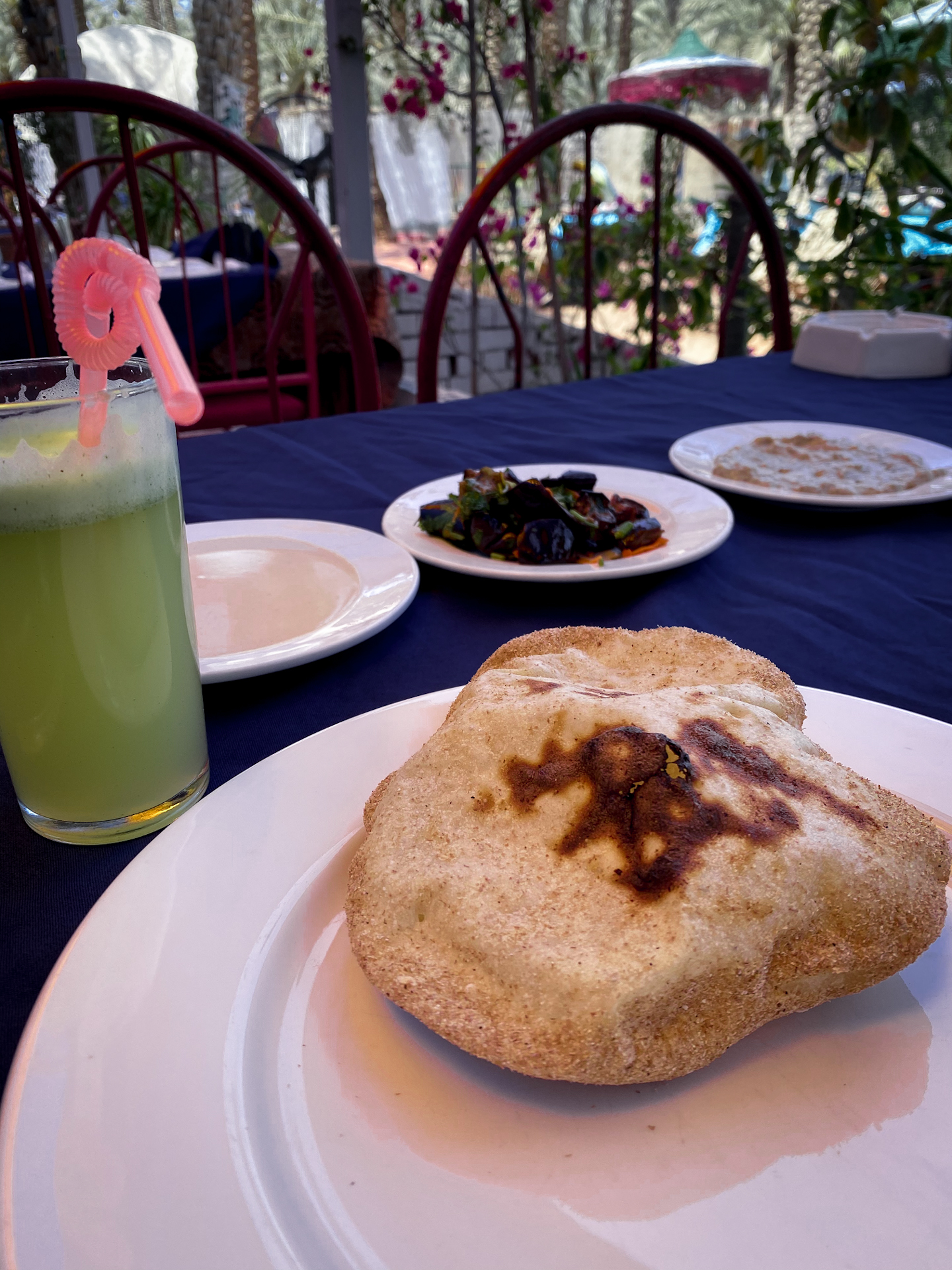 Fluffy Egyptian Bread in front of a glass of mint lemonade and three plates full of hummus, baba ganoush and olives.