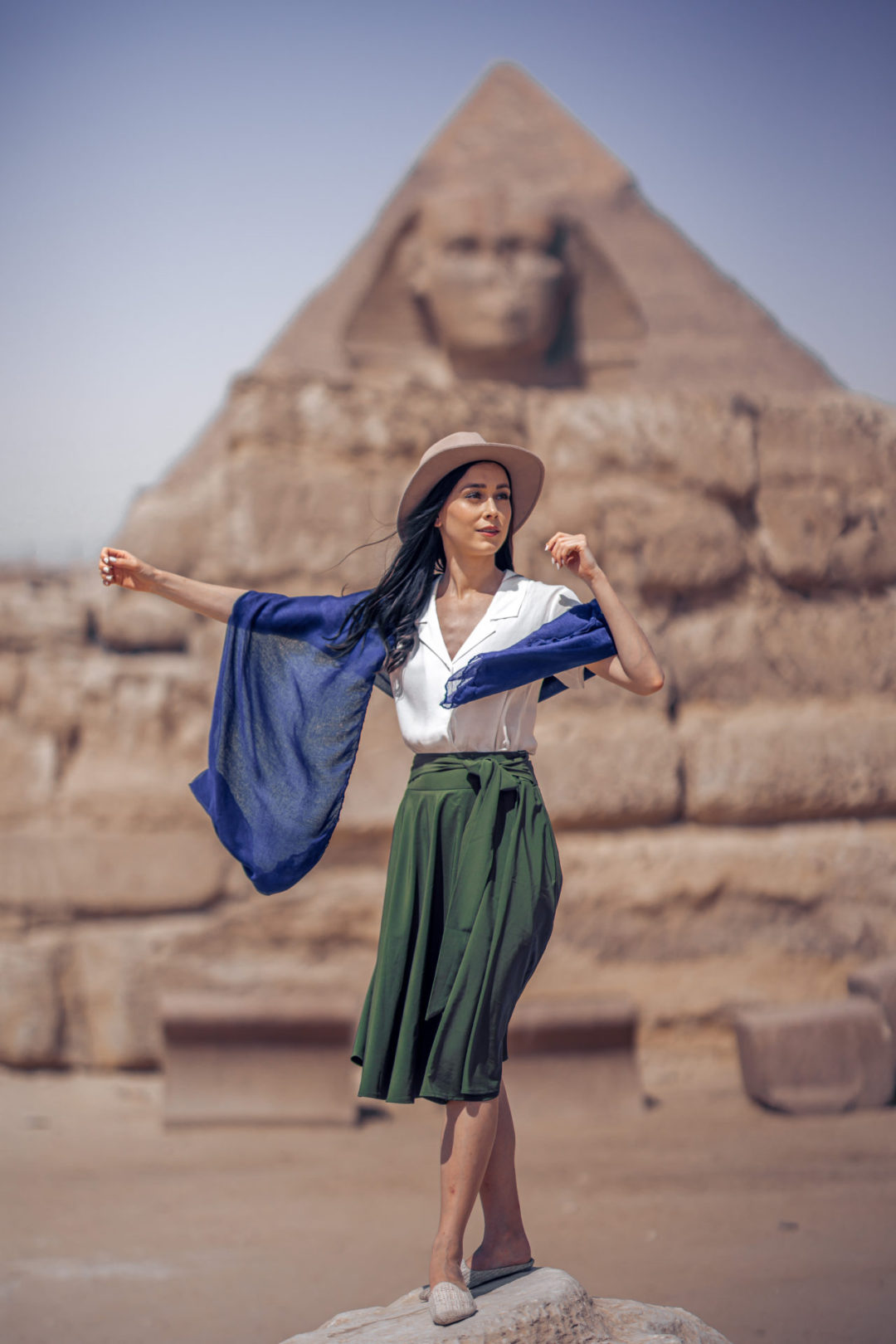 Jordan Gassner wearing an explorer hat, indigo scarf, white button down and green midi skirt in front of the Sphinx in Giza, Egypt