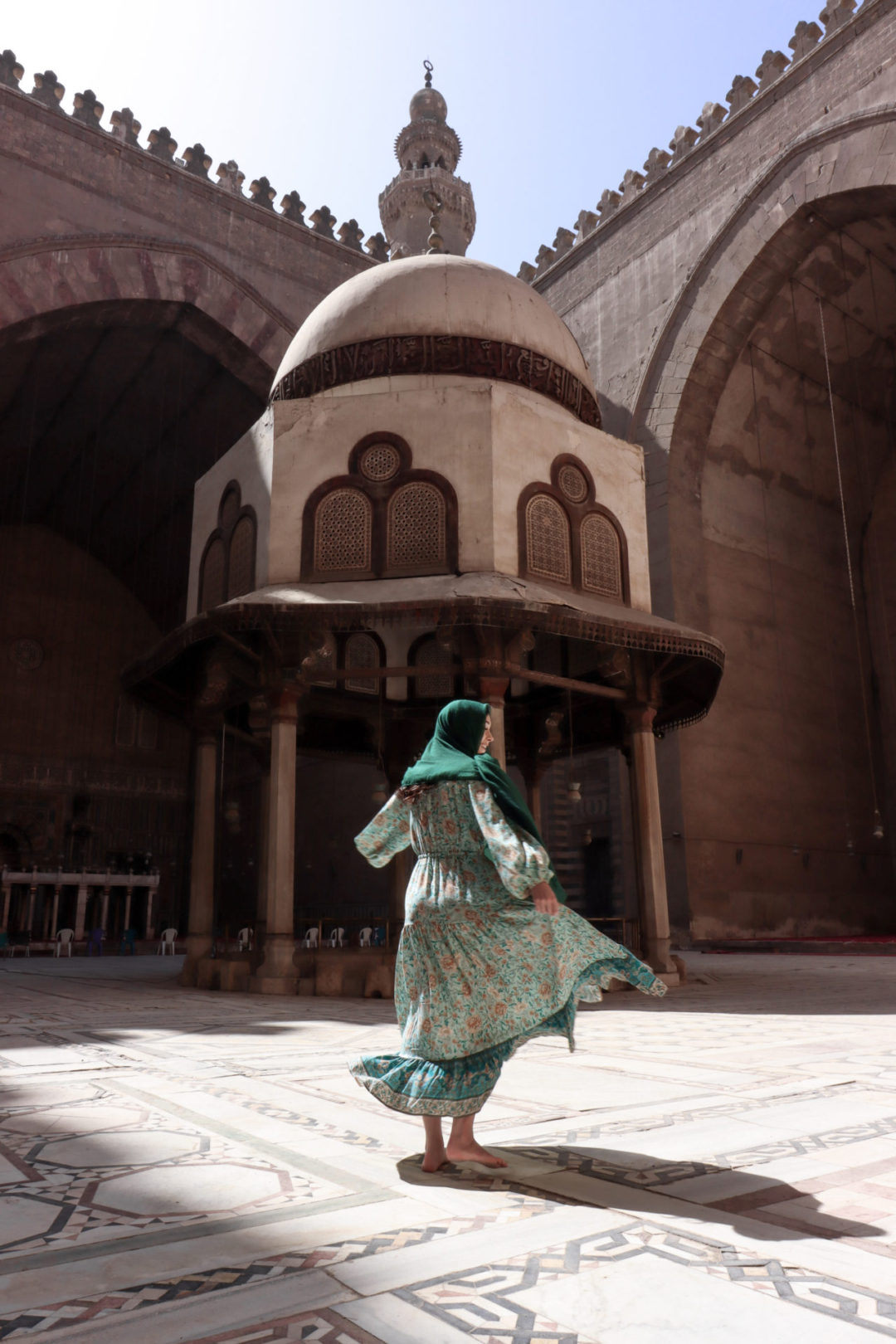 Jordan Gassner twirling in a turquoise dress and hunter green head scarf in the courtyard of the Mosque-Madrassa of Sultan Hassan in Cairo, Egypt