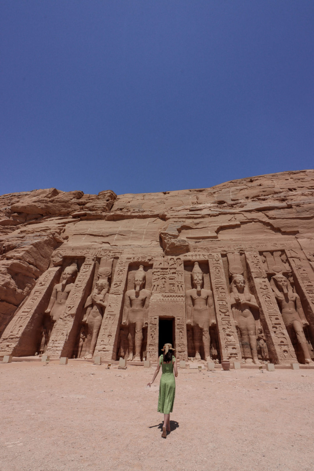 Top Ancient Sights in Egypt: Travel Blogger Jordan Gassner wearing a green dress and straw sunhat walking toward the secondary temple in Egypt's Abu Simbel