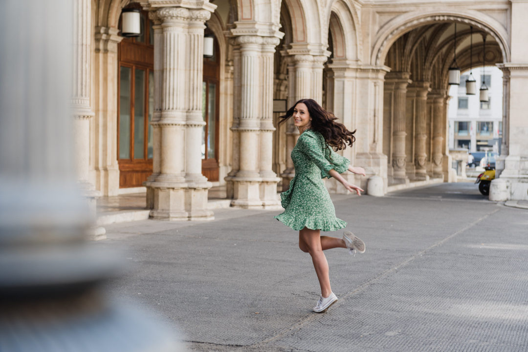 Jordan Gassner twirling in a green floral dress in front of the Vienna Opera House in Austria