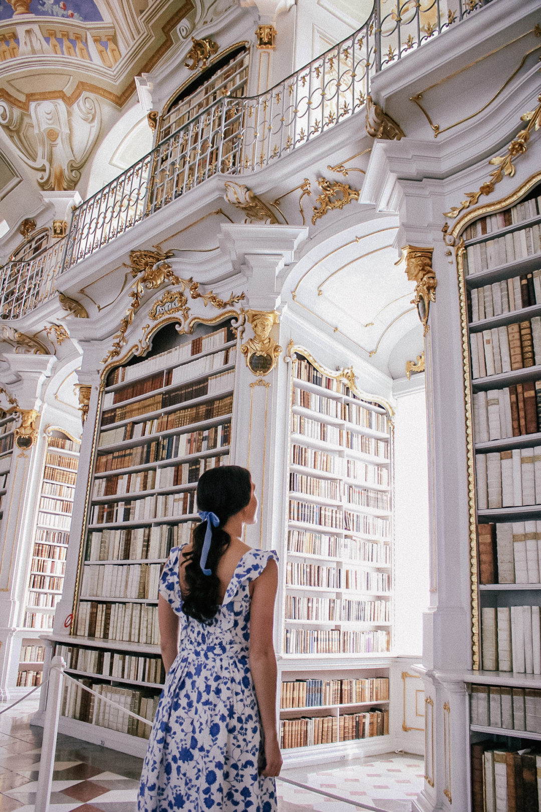 Travel Blogger Jordan Gassner taking a tripod photo as Belle from Beauty in the Beast and looking at a bookshelf at Admont Abbey in Austria