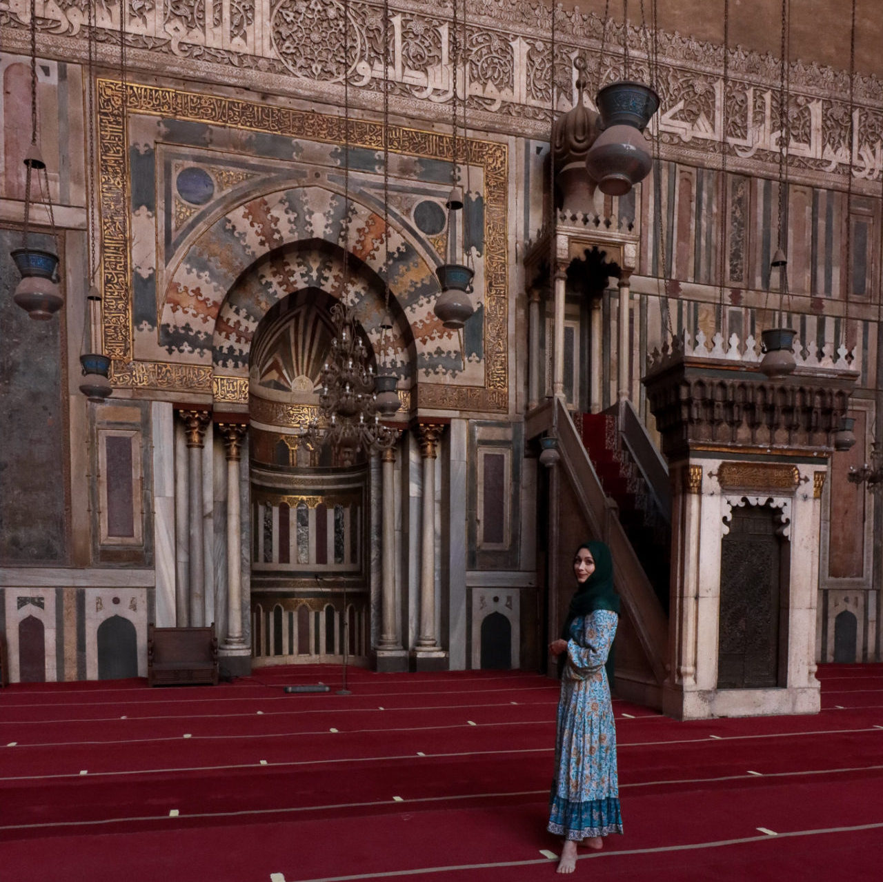 Jordan Gassner wearing a turquoise dress and hunter green head scarf in the front of the minbar at Madrassa of Sultan Hassan in Cairo, Egypt