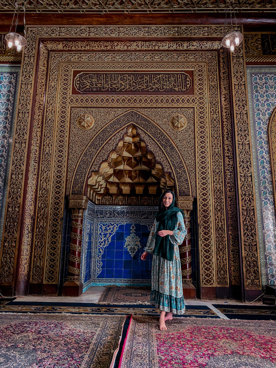 Jordan Gassner wearing a turquoise dress and hunter green head scarf inside the Cairo Mosque at the Manial Palace Museum