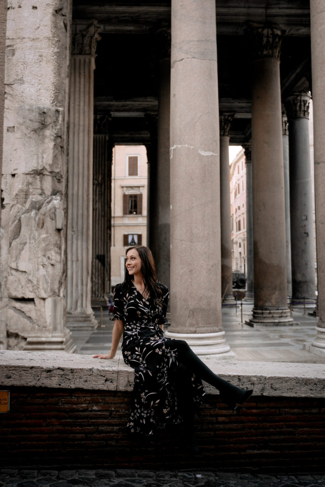 Jordan Gassner sitting in a black floral dress and smiling alongside the Pantheon in Rome, Italy