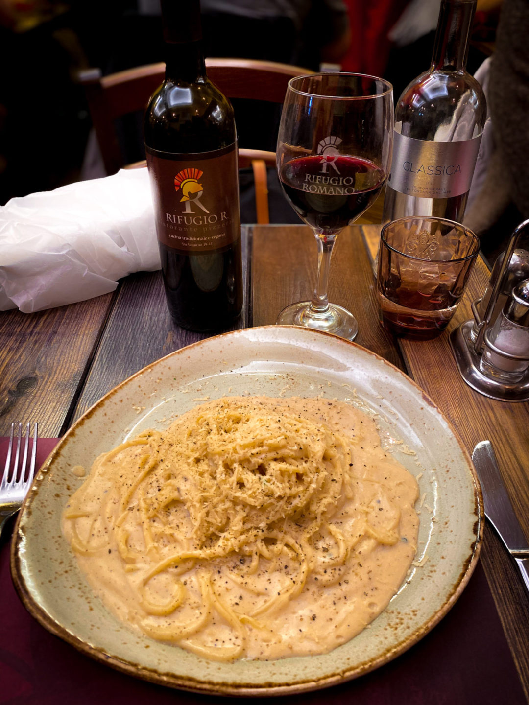 Vegan Cacio e Pepe from Rifugio Romano Restaurant in Rome, alongside a bottle and glass of their signature red wine