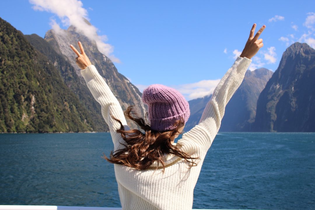 Visiting New Zealand: Travel Blogger, Jordan Gassner, throwing up peace signs from a boat tour through Milford Sound on New Zealand's South Island