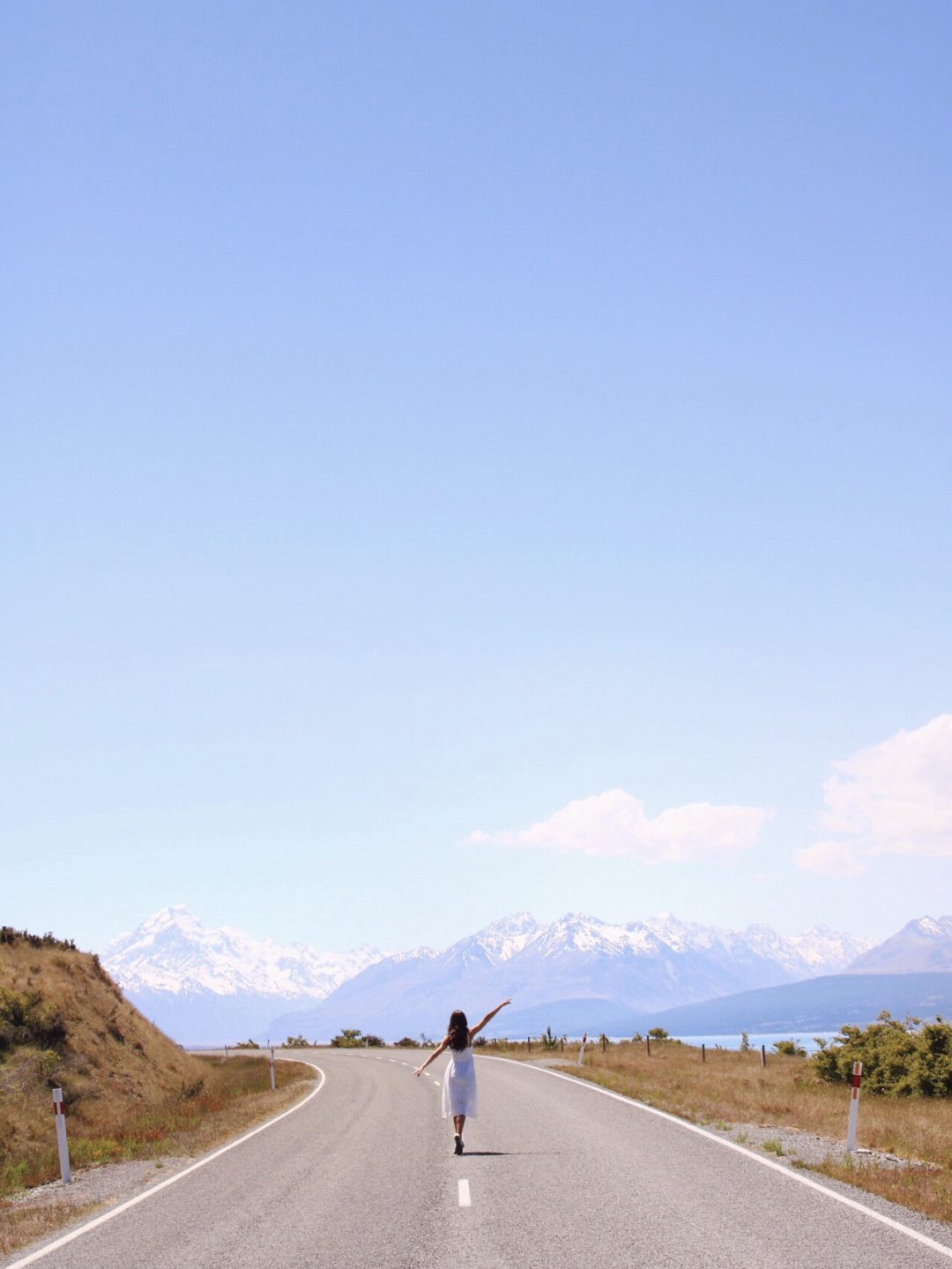 Visit New Zealand: Travel Blogger, Jordan Gassner wearing a white dress while walking along the main road to Mount Cook in New Zealand