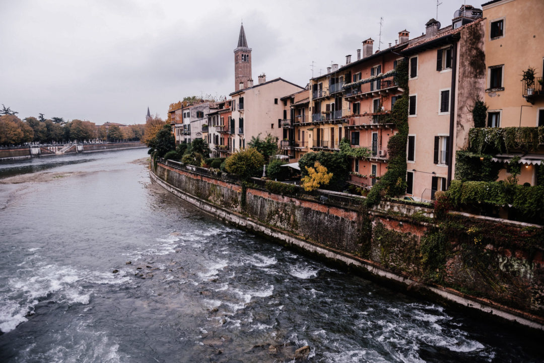 A row of orange, strawberry and cotton candy colored buildings standing along the Adige River in Verona, Italy
