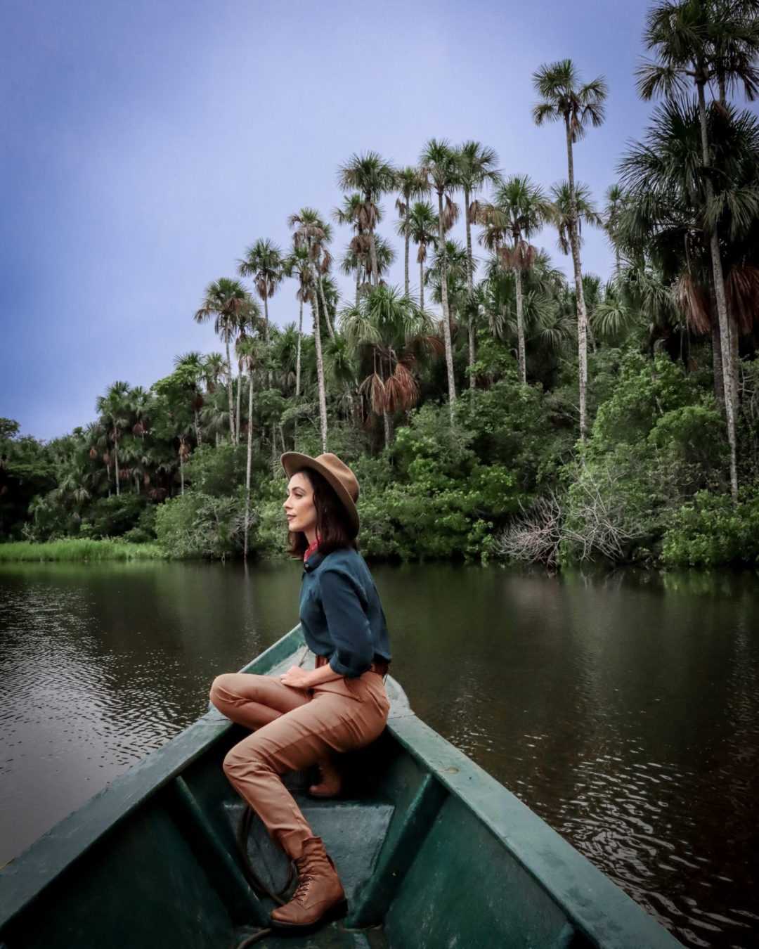 Travel Blogger Jordan Gassner wearing a vintage explorer outfit while looking out from a boat on Lake Sandoval in the Peruvian Amazon while staying at Inkaterra Reserva Amazonica