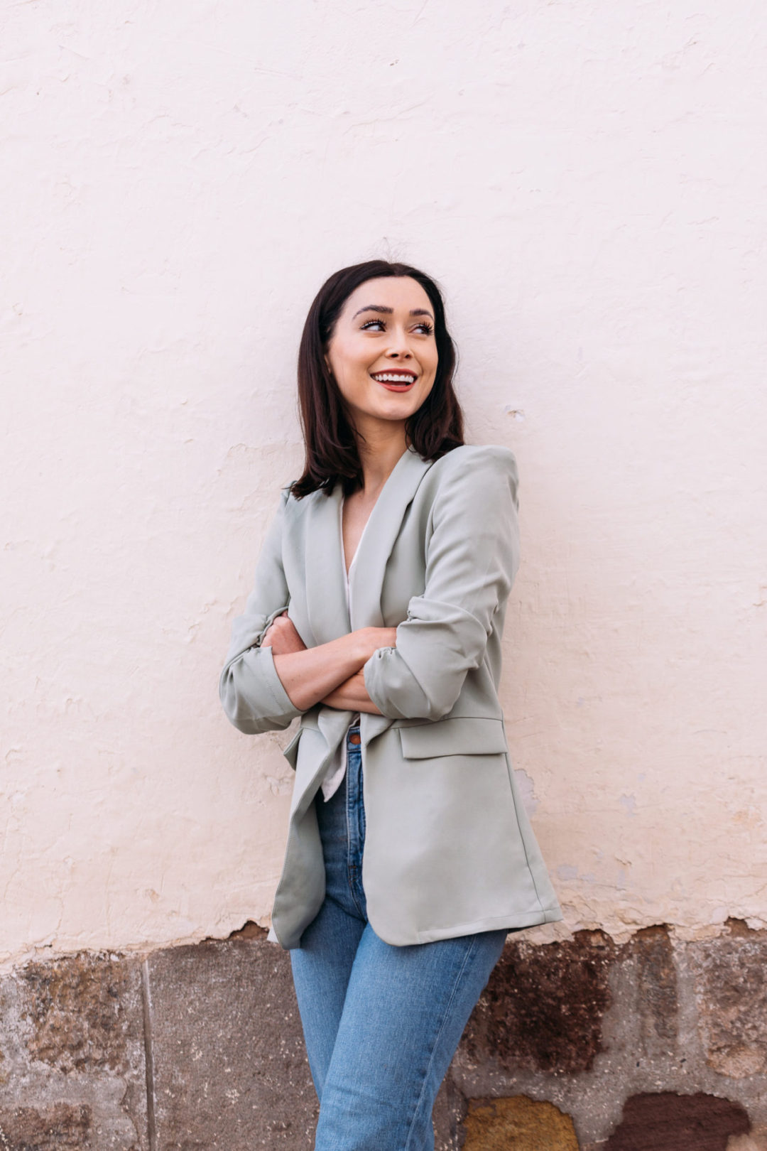 Jordan Gassner, with arms crossed, leaning against a cream stucco wall and smiling over her left shoulder
