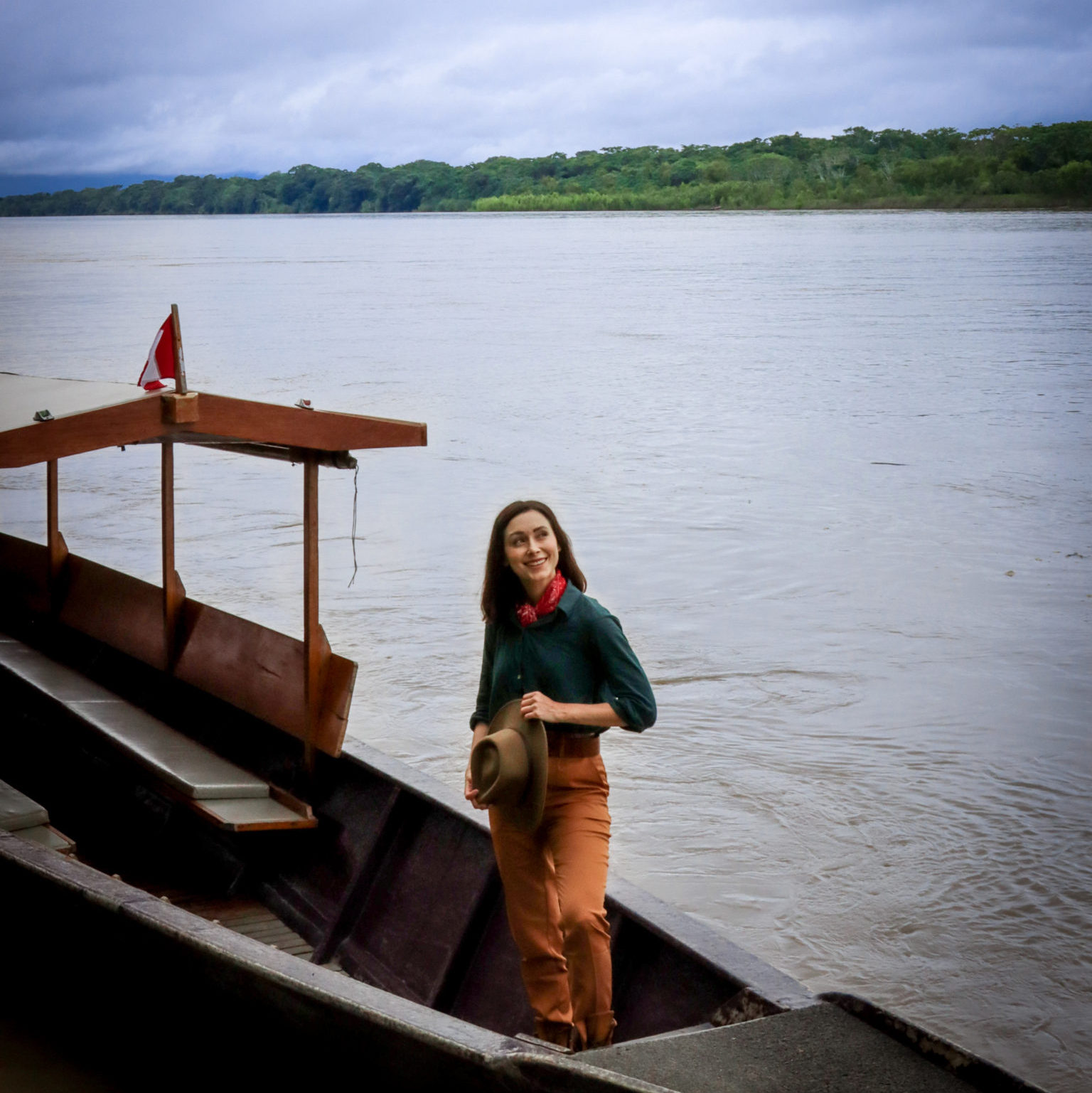 Travel Blogger, Jordan Gassner, wearing a vintage explorer outfit while standing and smiling in a long wooden motor boat at Inkaterra Reserva Amazonica in Puerto Maldonado, Peru, The Amazon
