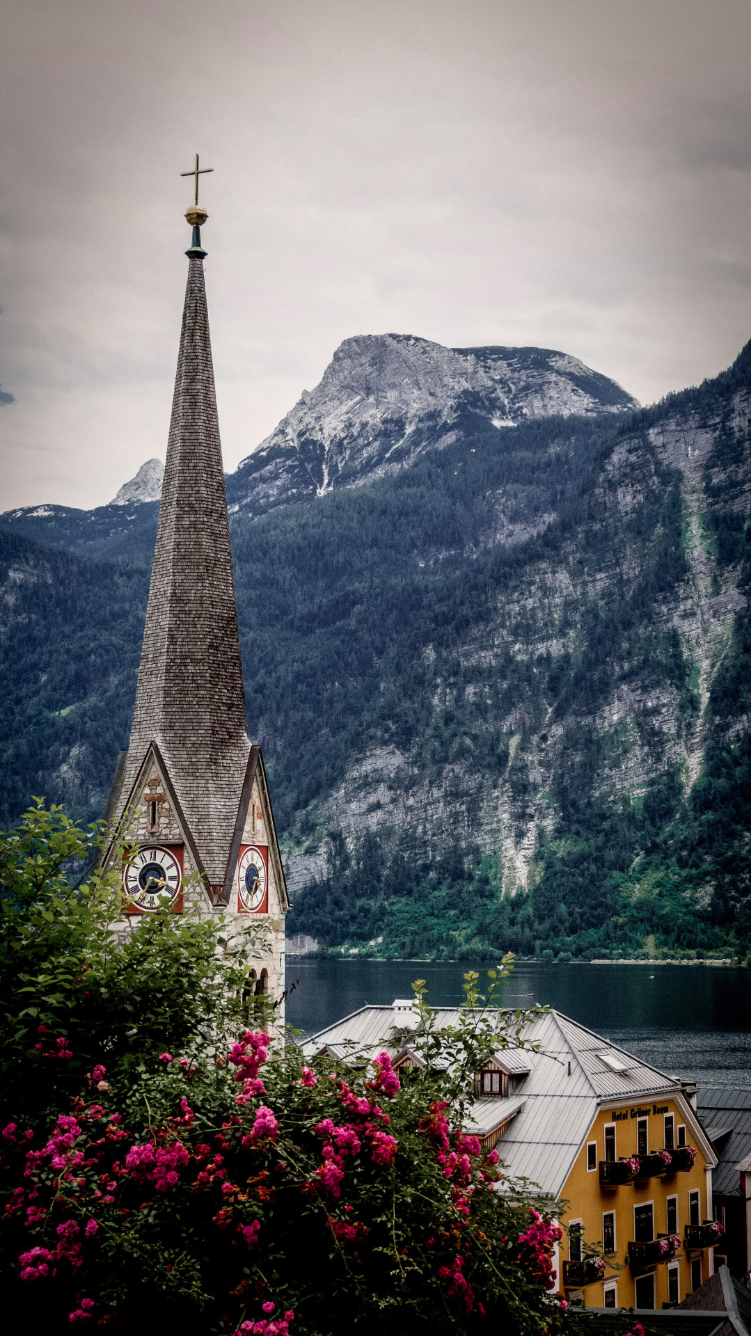 Yellow painted Seehotel Grüner Baum and a nearby clocktower spire in front of the lake view in Hallstatt, Austria