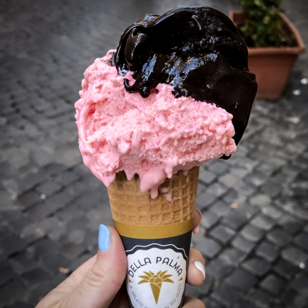 Close-up of a woman's hand holding an ice cream cone with vegan dark chocolate and strawberry gelato from Gelateria Della Palma in Rome, Italy
