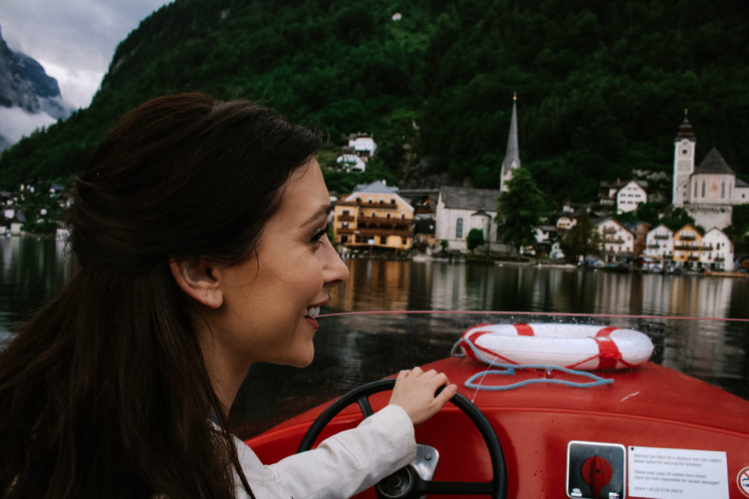 Jordan Gassner smiling and driving an electric boat on Lake Hallstatt, with the historic village just behind