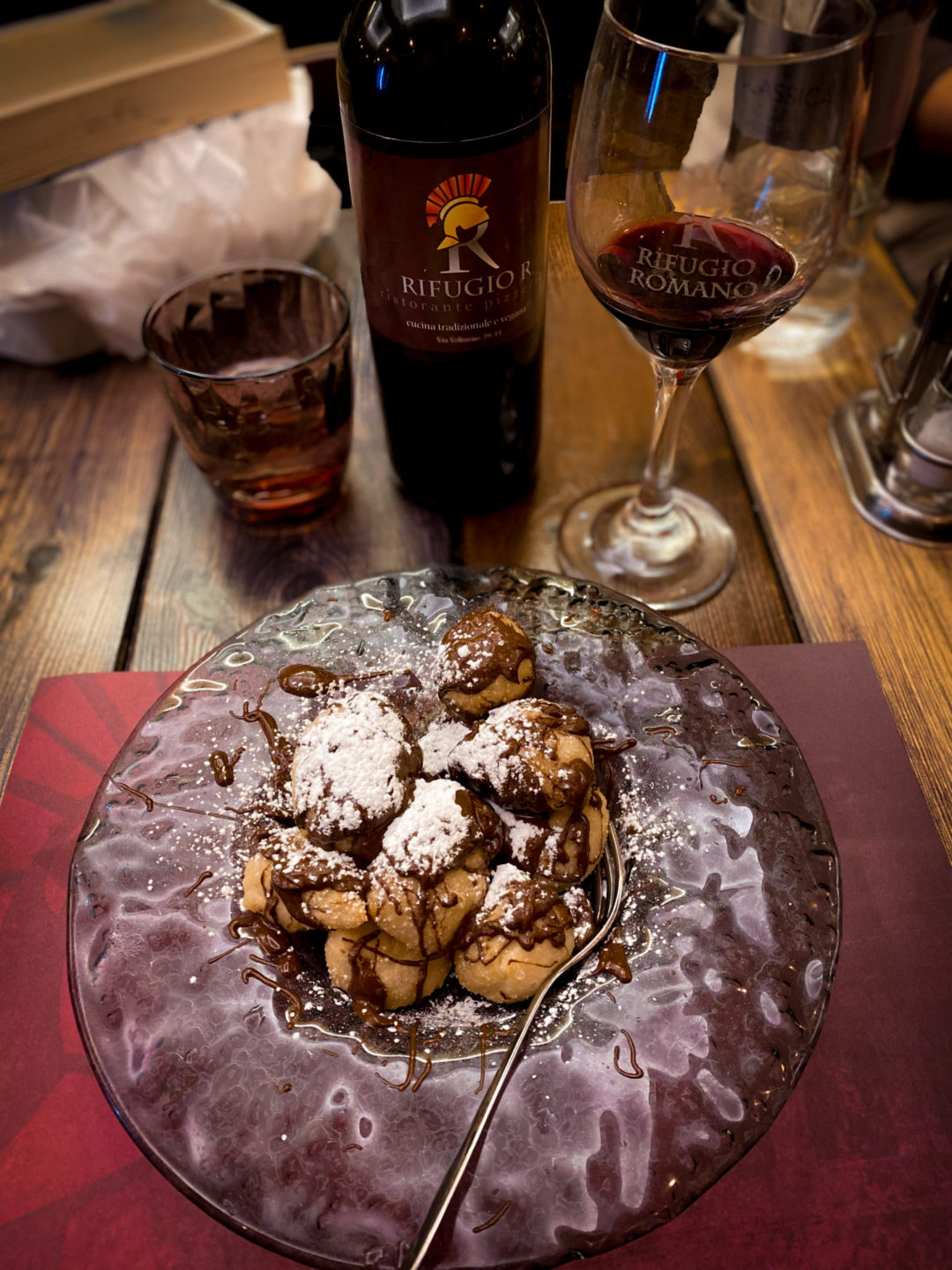 Zoccolette Romane con Nutella on a clear glass plate and next to a bottle and glass of red wine on a table at Rifugio Romano Restaurant in Rome, Italy