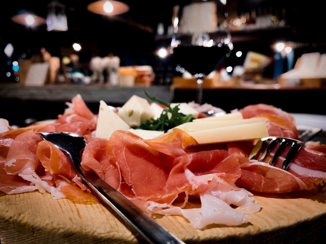 Various gourmet cured meats and glass of red wine inside of a restaurant