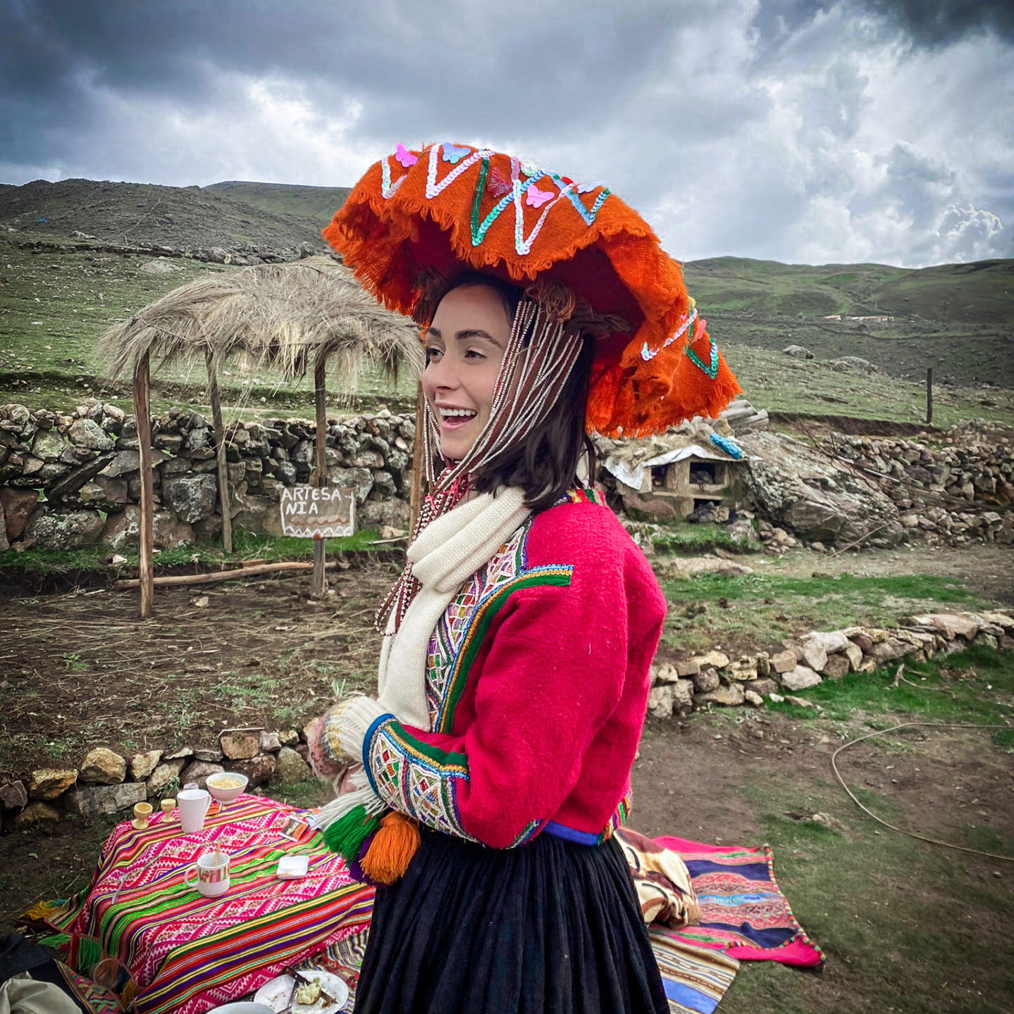 Female Travel Blogger smiling off-camera and wearing a traditional Quechua skirt, jacket and hat in the remote Peruvian Andes at a local picnic 