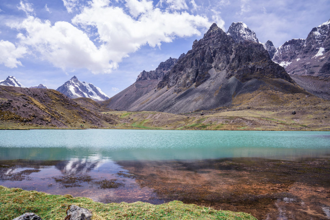 A clear turquoise glacial lake in front of the jagged mountain landscape of the Peruvian Andes on the Ausangate 7 Lakes Trek near Cusco, Peru