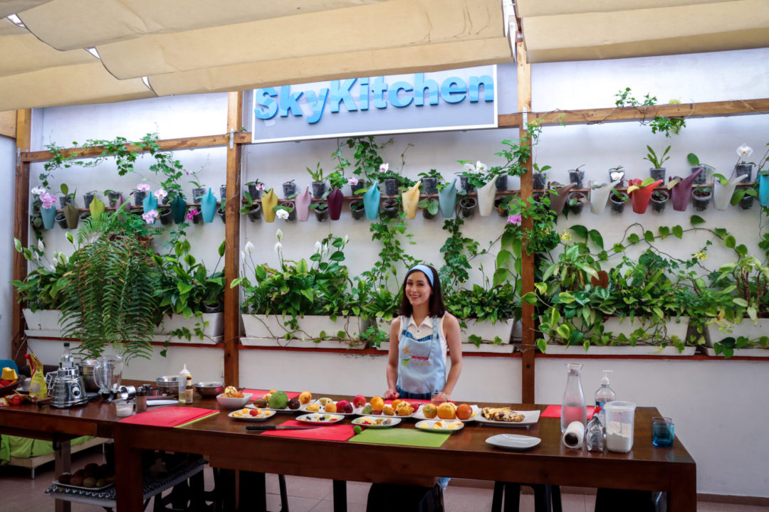 Travel Blogger Jordan Gassner smiling under the SkyKitchen cooking class sign and potted plans wall inside their Lima high-rise studio