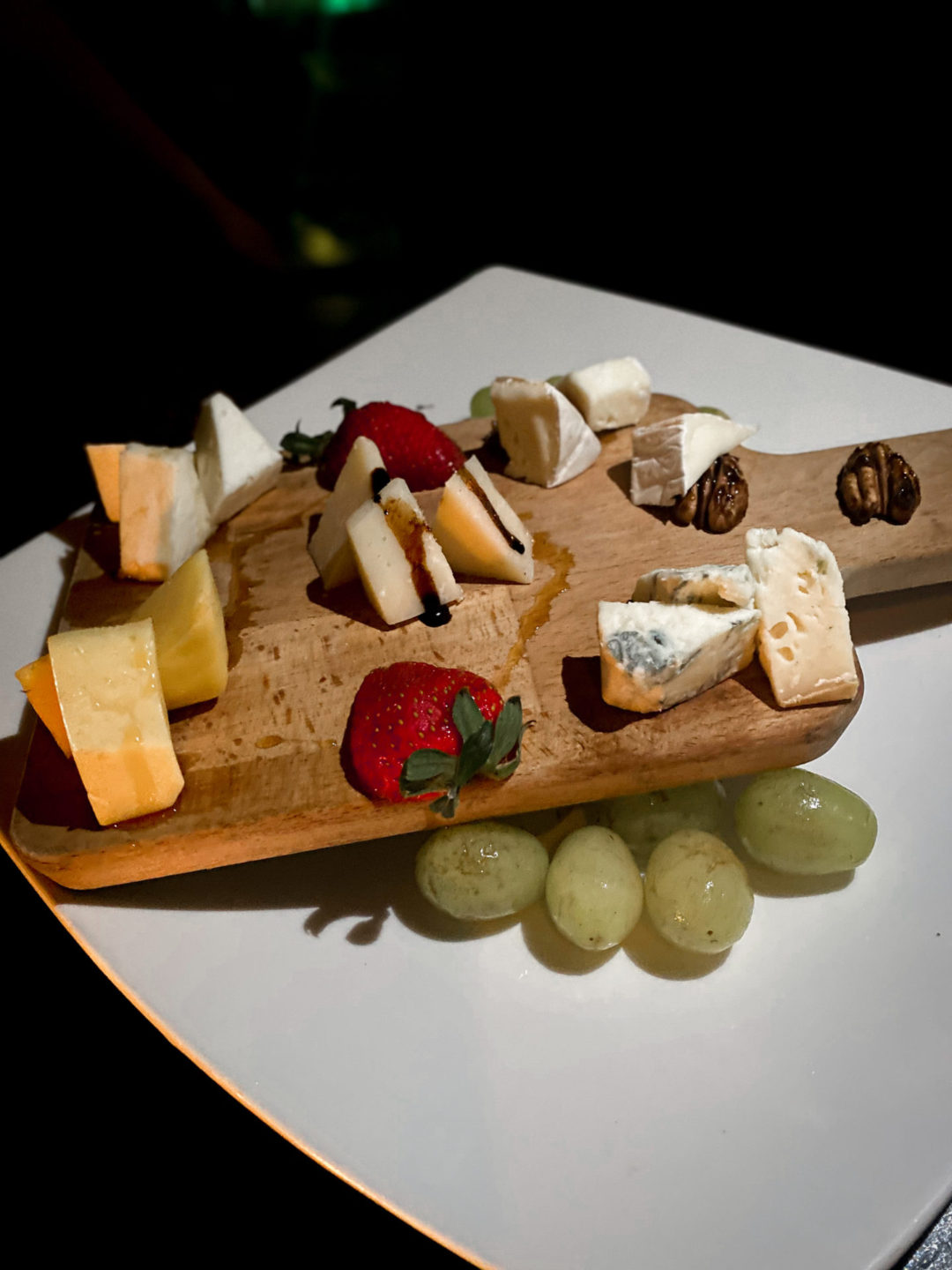 Wooden serving board with strawberries, green grapes, walnuts and an array of vegan cheese slices including blue cheese and parmesan