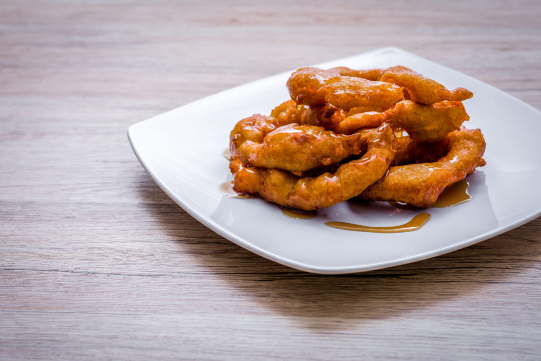 A plate of warm picarones drizzled in chocolate sauce on a white plate sitting on a wood countertop at SkyKitchen Cooking School in Lima, Peru