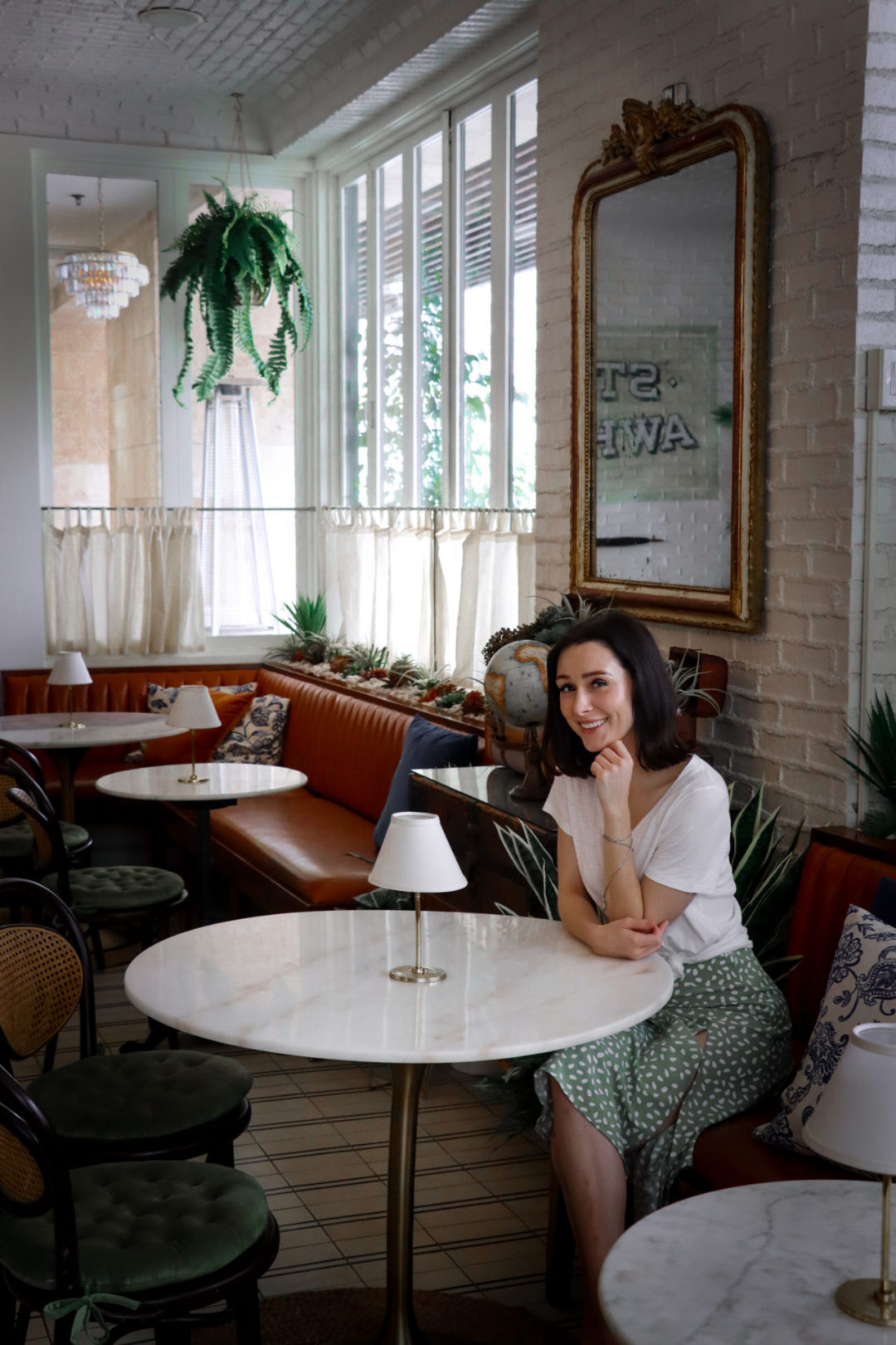Travel Blogger Jordan Gassner wearing a mint green skirt and white shirt sitting at a marble table top inside Ella Beverly Hills Restaurant