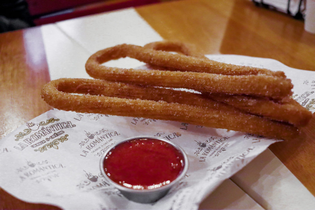 Three rounded churos sit next to a goblet of strawberry sauce on cooking paper titles "La Romantica"