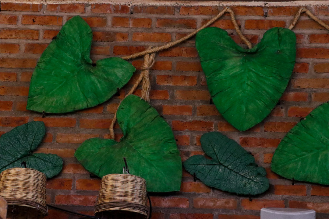 Heart-shaped palm fronds connected by "rope branches" hanging on a red brick wall