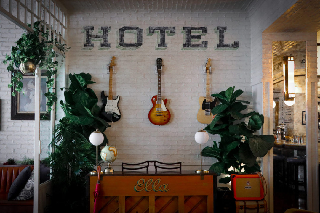 Underneath the hand painted blue and green "HOTEL" text lining the white brick walls inside Ella Restaurant are three classic guitars, an amplifier and a piano with painted "Ella" text in front.