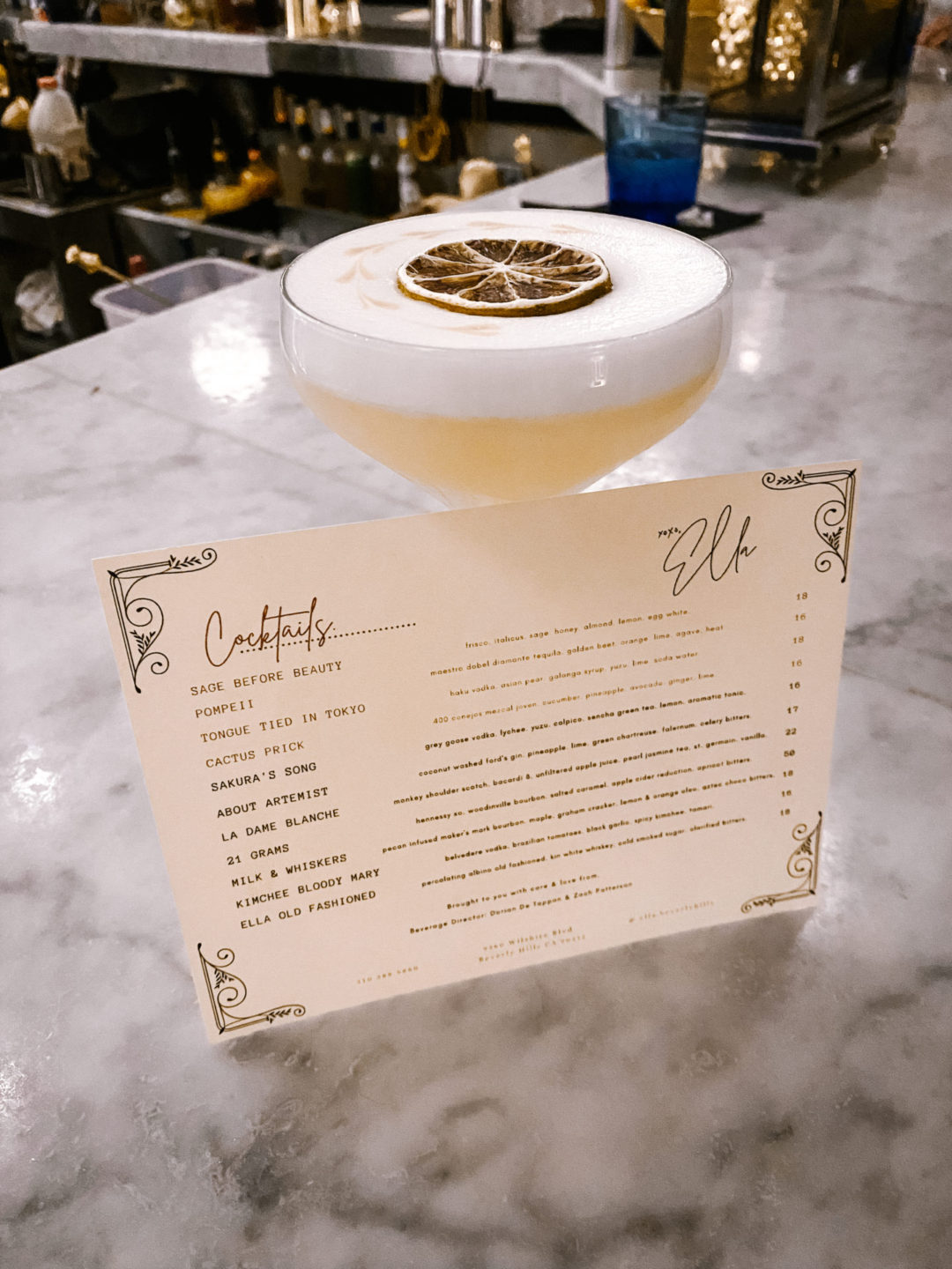 Ella Beverly Hills' cocktail list propped up against a drink on their marble top bar.