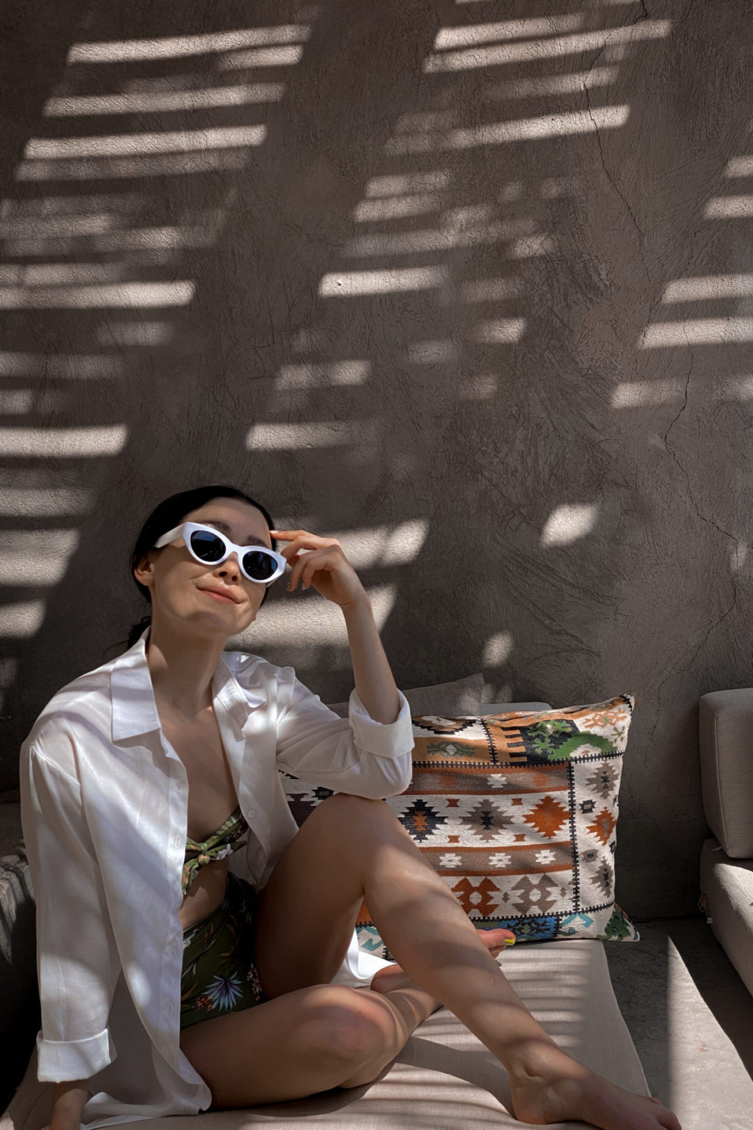 What to Wear in Egypt: Travel Blogger Jordan Gassner wearing white sunglasses, a white 3/4-length sleeve button-down cover-up and a tropical leaf high waisted bikini while lounging on an outdoor chair in the shade in El Gouna, Egypt