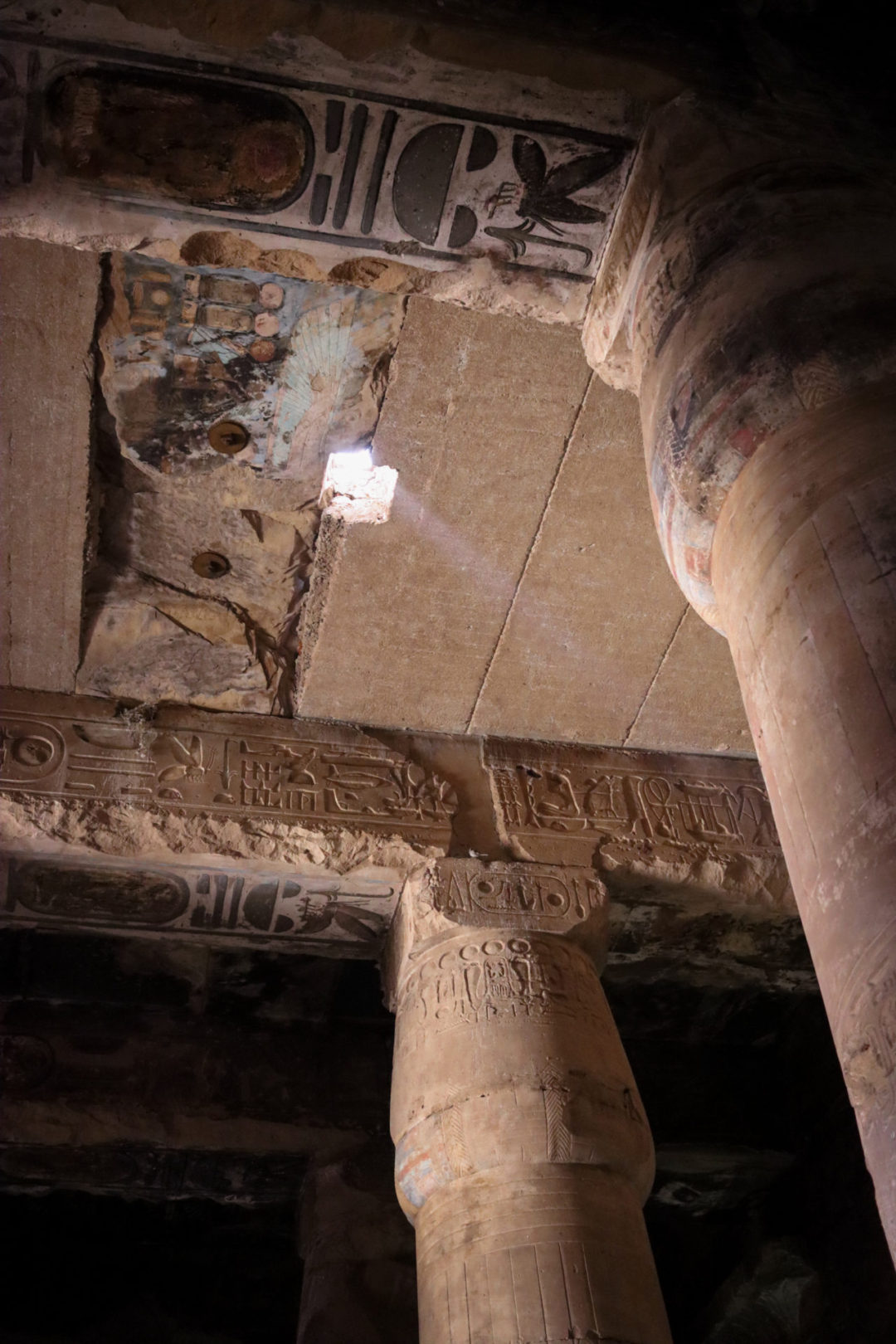 Top Ancient Sights in Egypt: A low angle view up at the inner roof of Abydos Temple, where the ceiling is cracked with light shining through, smoke marks, and ancient graffiti, some of which, due to its writing over past inscriptions, even resembles modern day transportation.