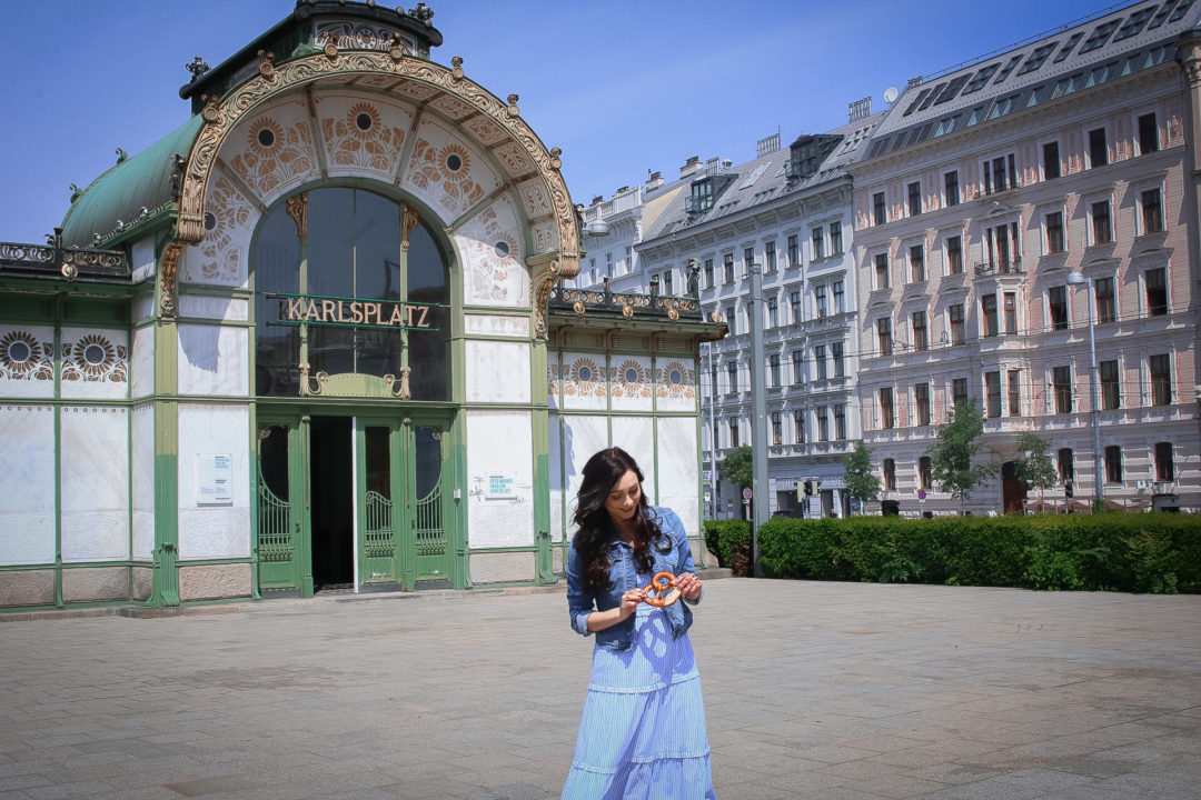 Vienna Travel Guide: Travel Blogger Jordan Gassner holding a pretzel in front of the old Karlsplatz Stadtbahn Station