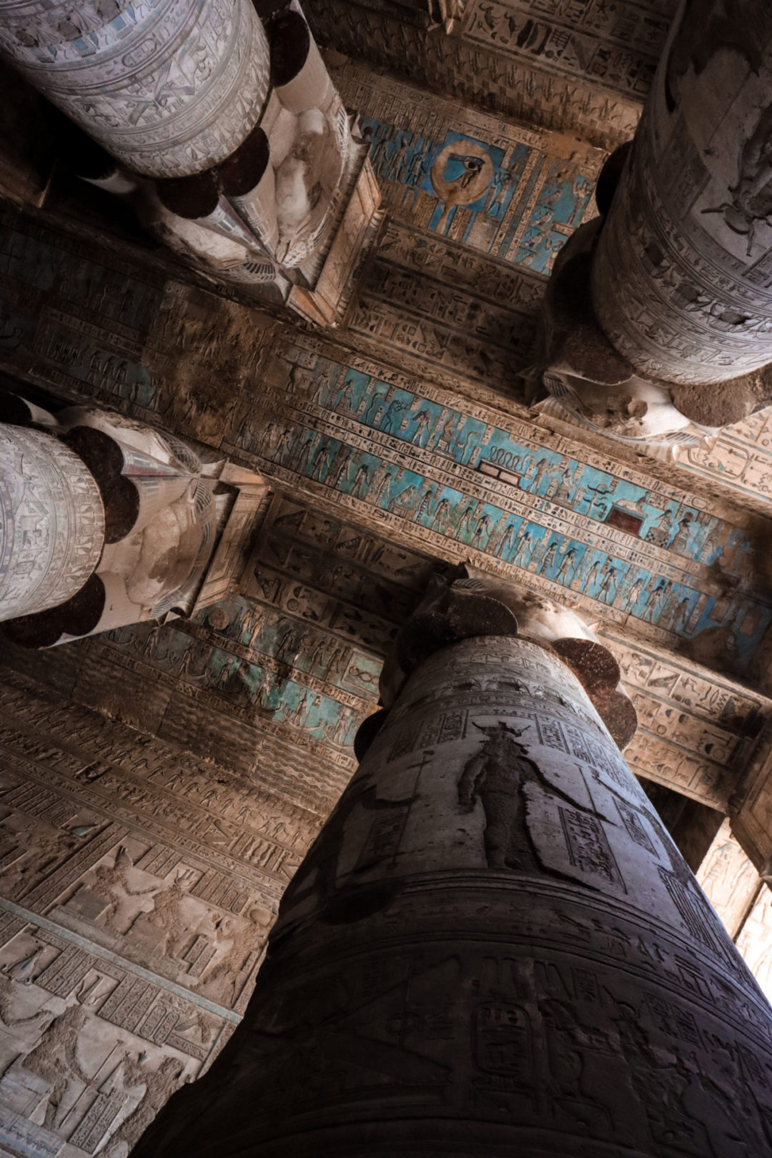 A view overhead at Egypt's Dendera Temple's blue-colored heiroglyph ceiling being supported by columns decorated with the image of the ancient goddess Hathor