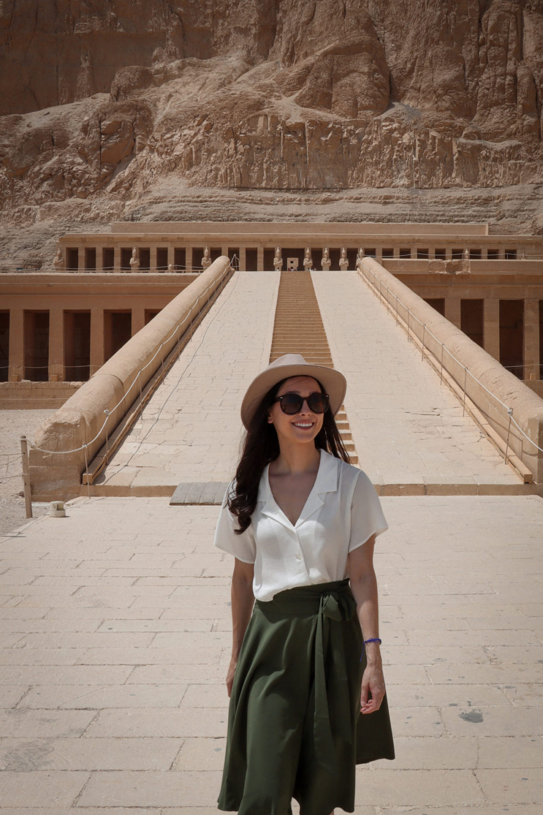 Travel Blogger Jordan Gassner walking with a smile directly in front of the empty ramp leading up to the second level of Luxor's ancient Mortuary Temple of Hatshepsut located along its west bank.
