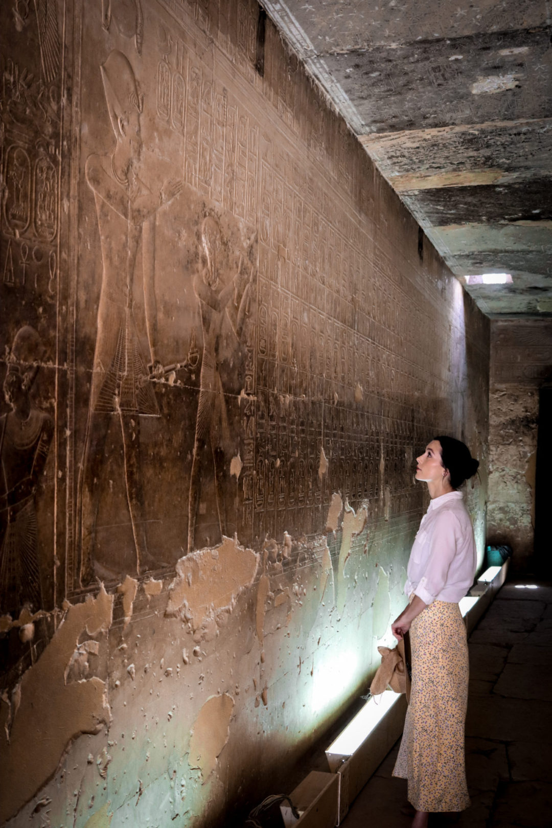 Travel Blogger Jordan Gassner wearing a yellow skirt, white button up shirt and straw hat staring up at the ancient hieroglyphs known as the Abydos Table