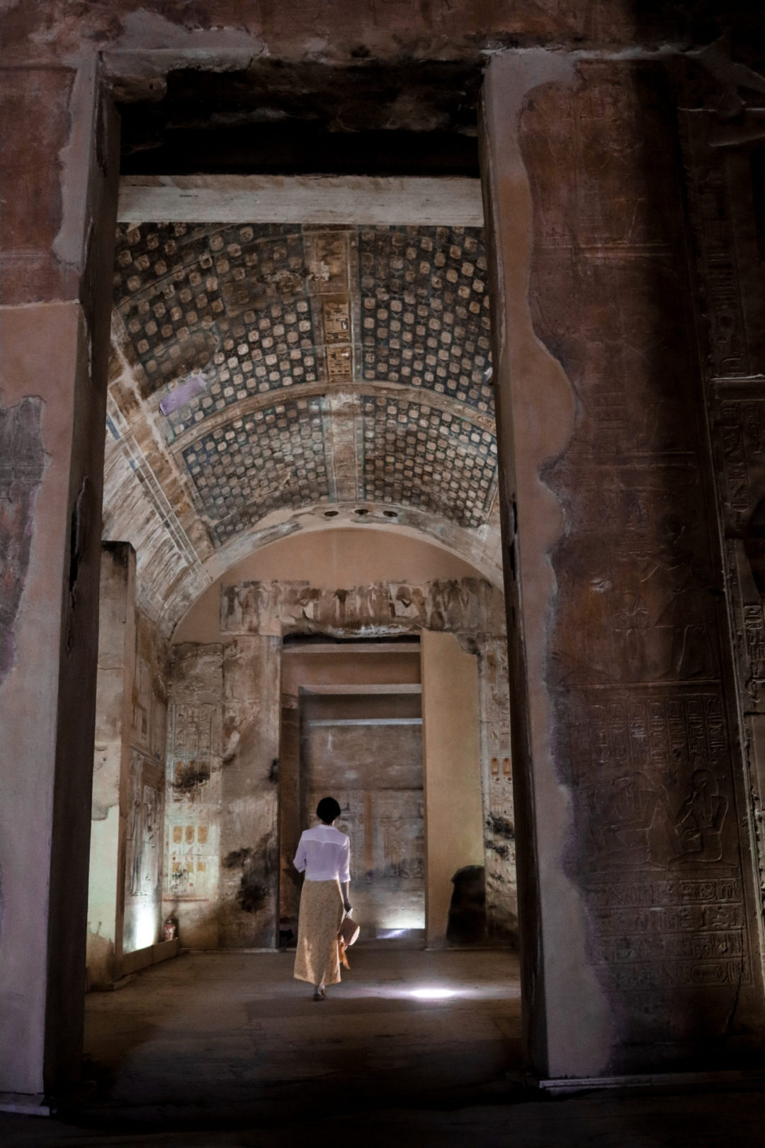 Travel Blogger Jordan Gassner wearing a yellow skirt, white button up shirt and straw hat walking through one of the small side temples inside Abydos Temple in Egypt