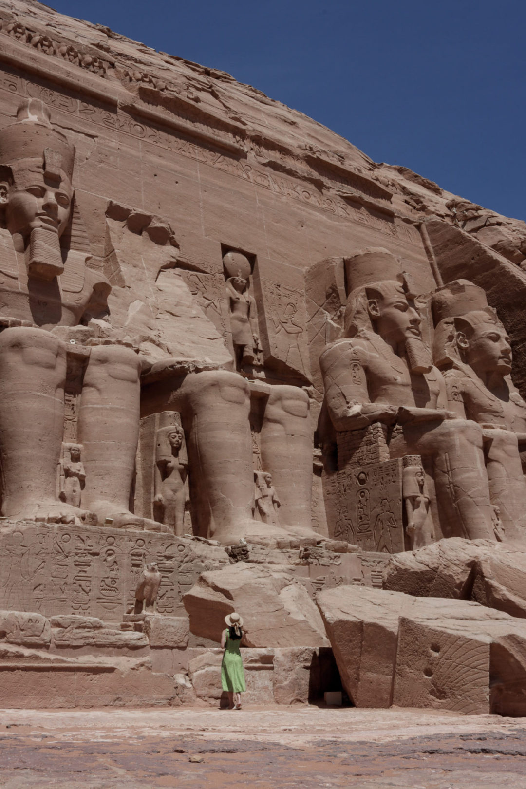 Travel Blogger Jordan Gassner wearing a green dress staring up at the four massive sitting statues of Ramses II at Abu Simbel Temple in Egypt