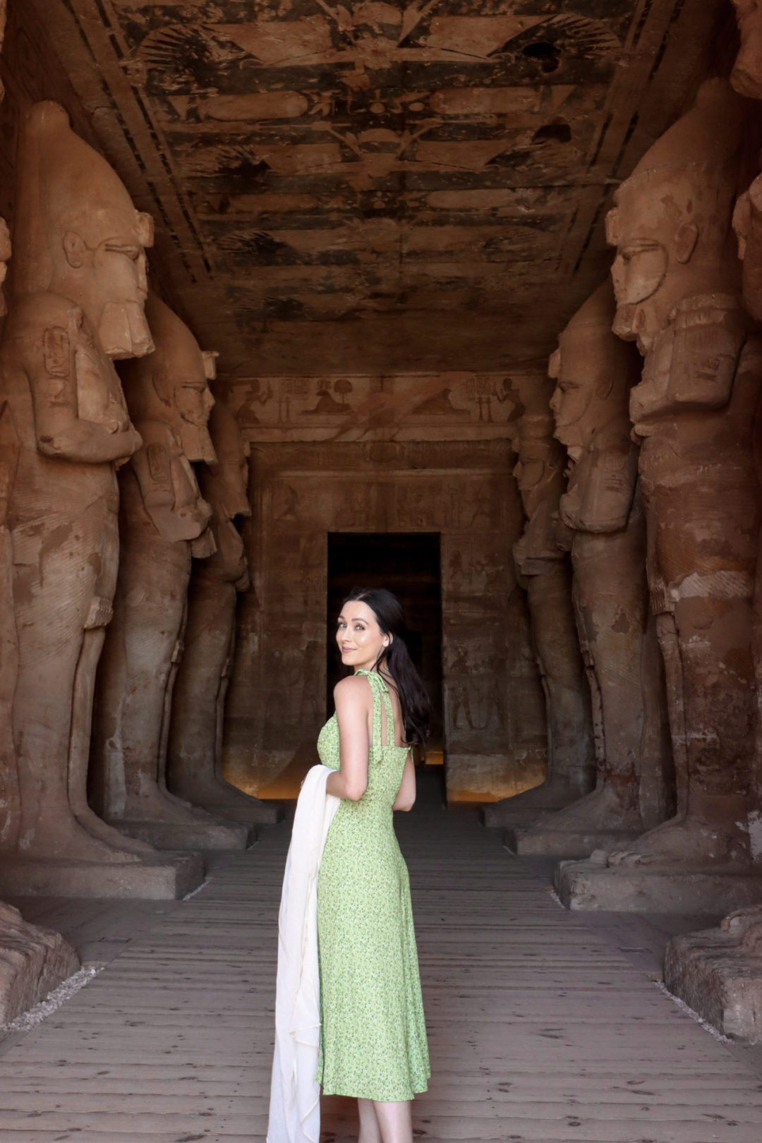 Top Ancient Sights in Egypt: Travel Blogger Jordan Gassner wearing a green dress and holding a green scarf looking back at camera inside the main temple of Abu Simbel Temple in Egypt