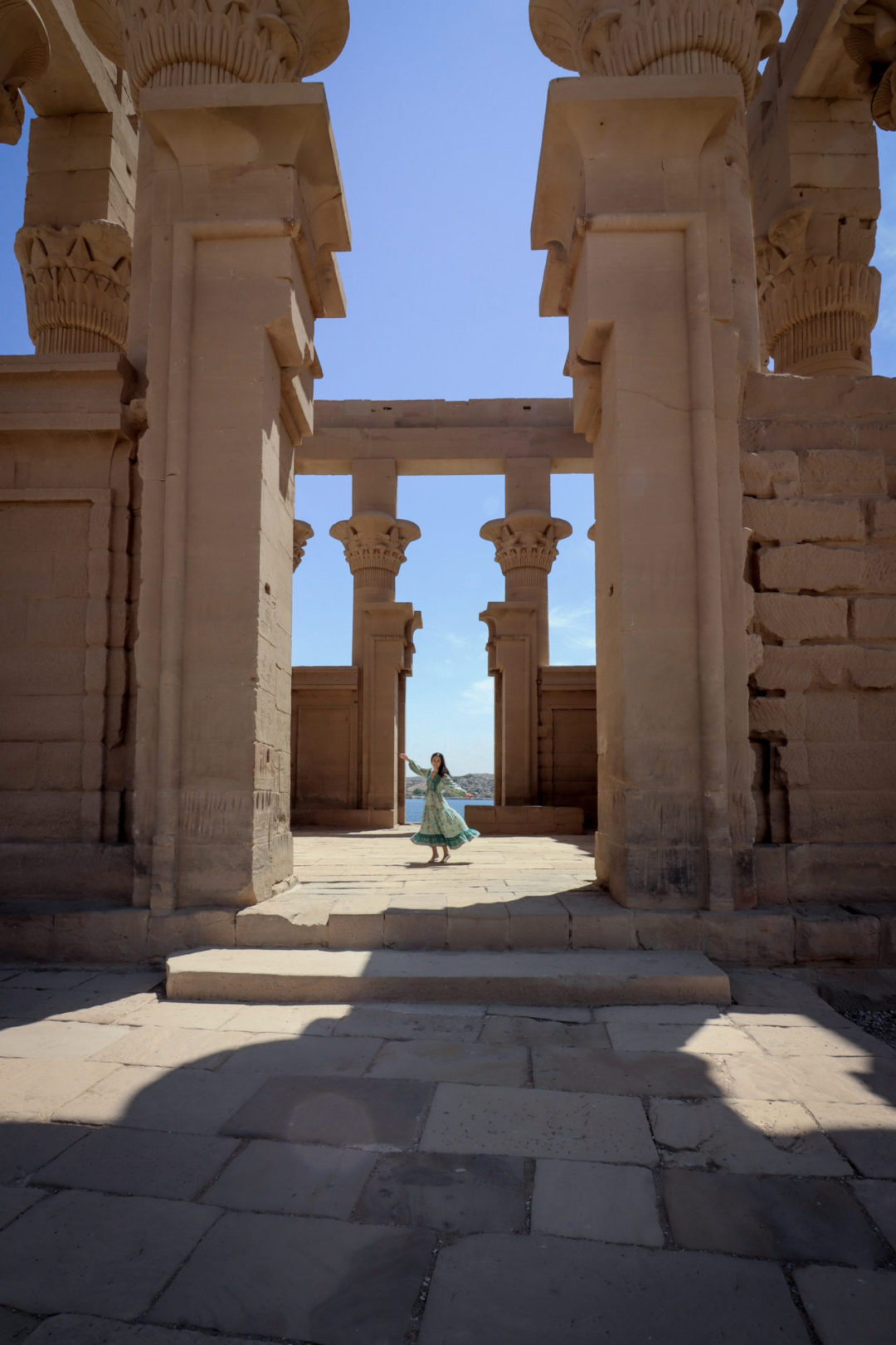 Travel Blogger Jordan Gassner wearing a long sleeve blue patterned maxi dress and twirling in the Philae Temple ruins on Philae Island in Aswan, Egypt