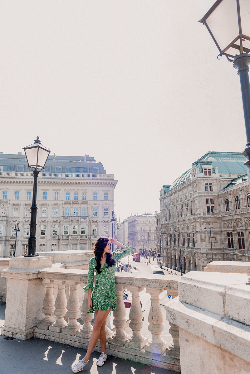 Vienna Travel Guide: Travel Blogger Jordan Gassner fixes her hair while leaning against a balcony overlooking the Vienna State Opera House