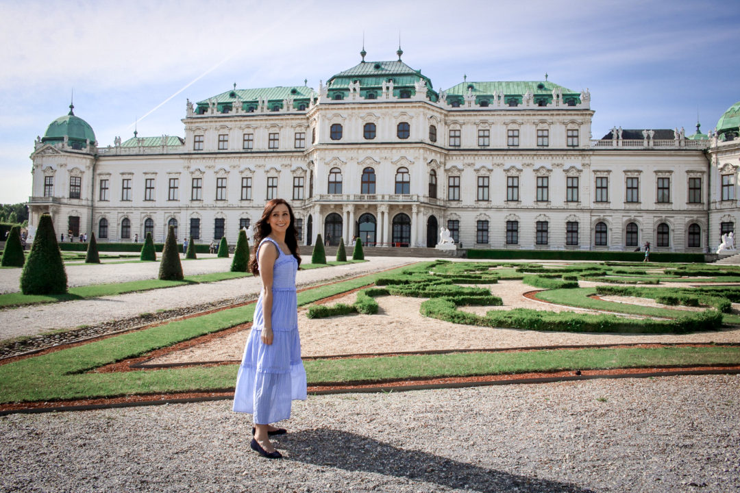 Travel Blogger Jordan Gassner taking a few tripod travel photos of herself smiling in front of Belvedere Palace in Vienna, Austria