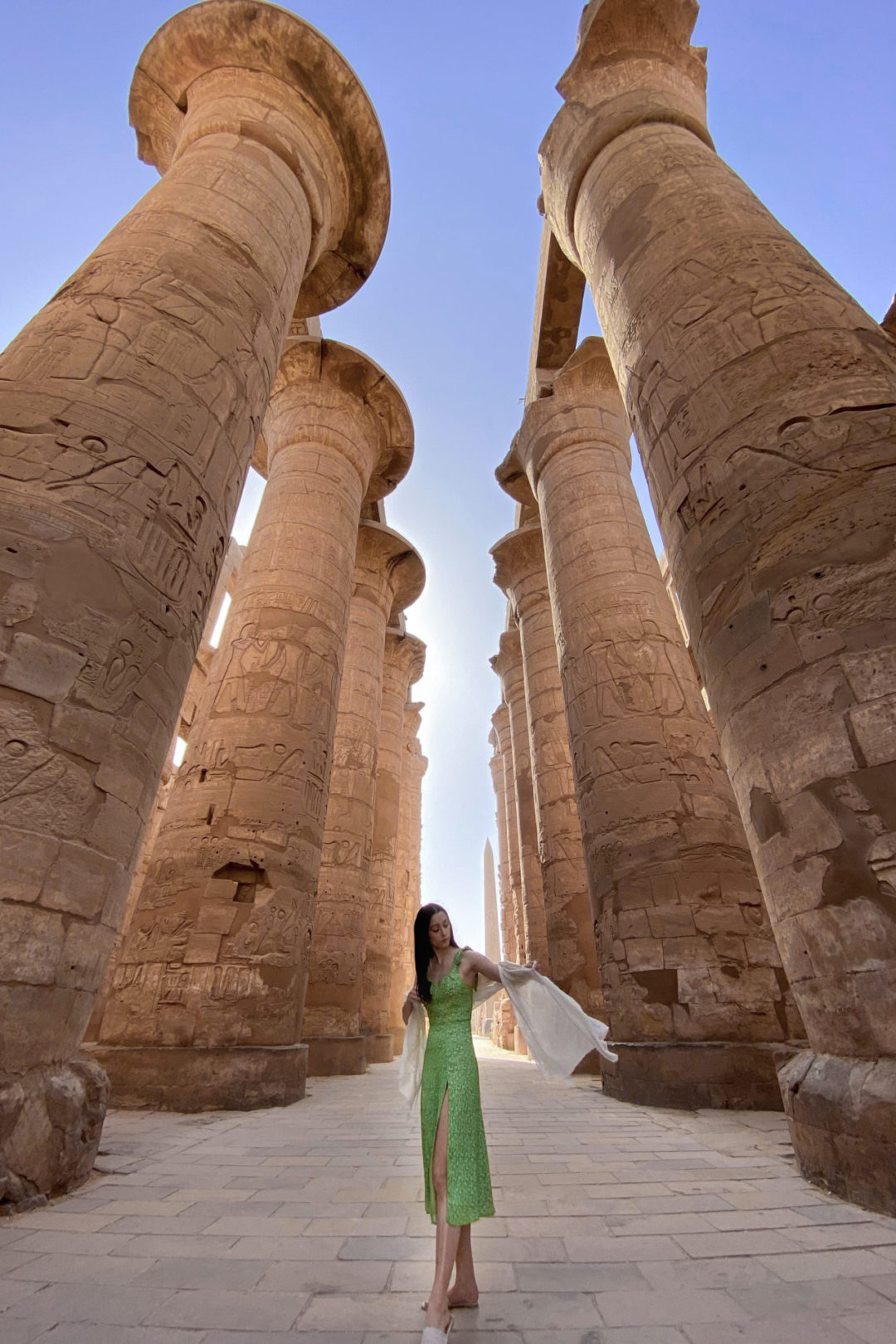 Top Ancient Sights in Egypt: Travel Blogger Jordan Gassner wearing a green dress and fixing a cream scarf on her arm while standing between a colonnade at Karnak Temple in Luxor, Egypt
